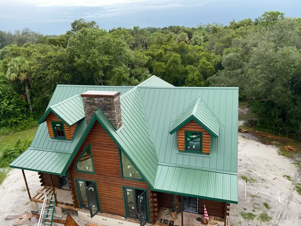 Green standing-seam metal roof on a log-style home under construction.