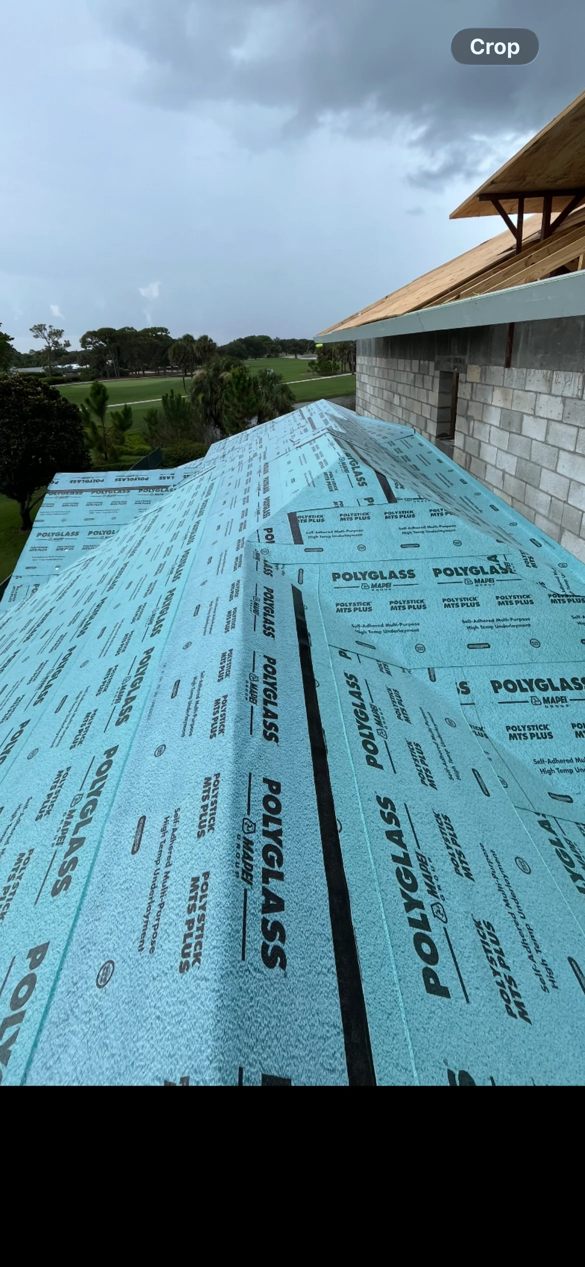 Blue Polyglass Polystick MTS Plus underlayment covering a sloped roof beside an unfinished masonry wall.
