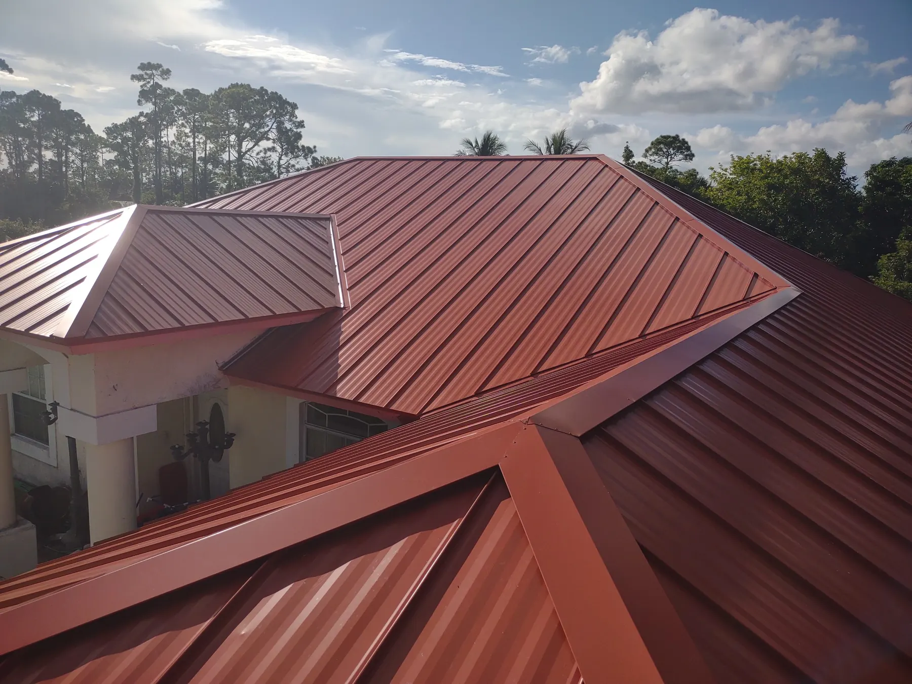 Close elevated view of a completed red standing-seam metal roof with multiple hips.