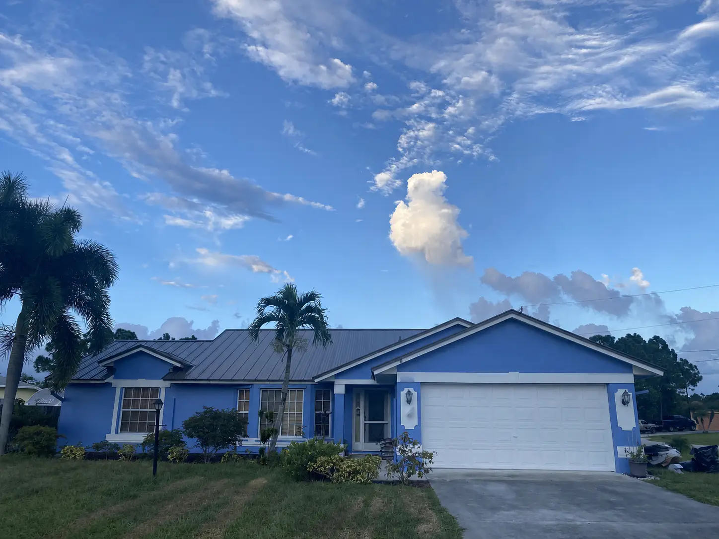 Silver standing-seam metal roof on a blue single-story home beneath a bright sky.