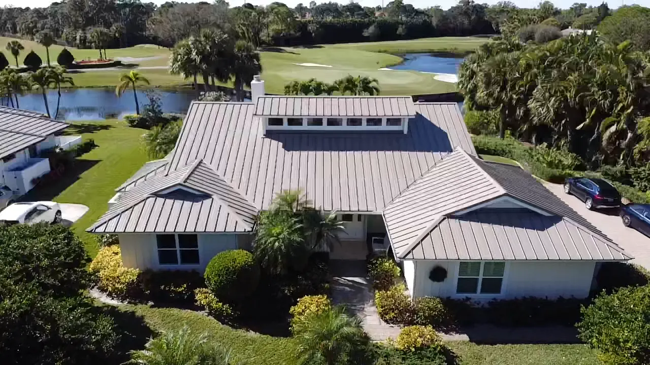 Aerial view of a completed white metal roof on a home beside a lake.
