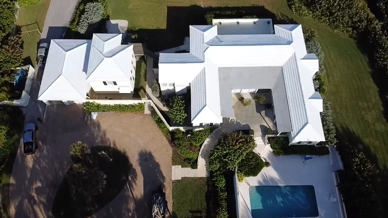 Aerial view of a large waterfront home with a completed white metal roof.