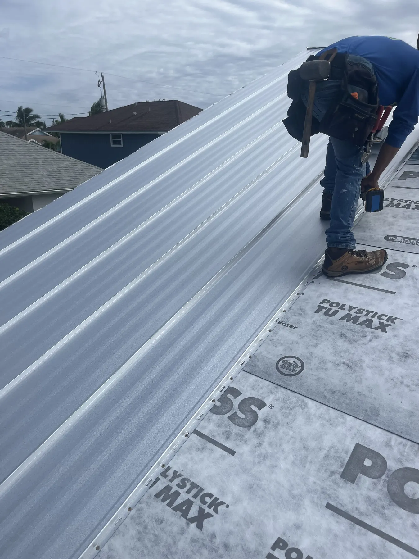 Roofing worker fastening a white metal roof panel over synthetic underlayment.
