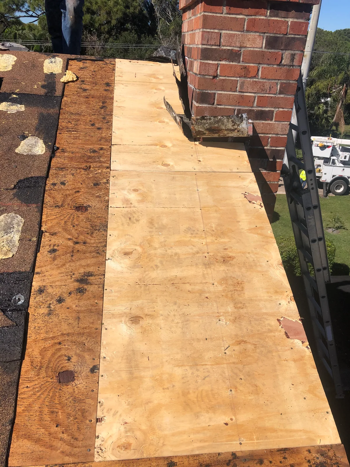 New plywood roof decking installed beside the brick chimney where damaged wood was removed.