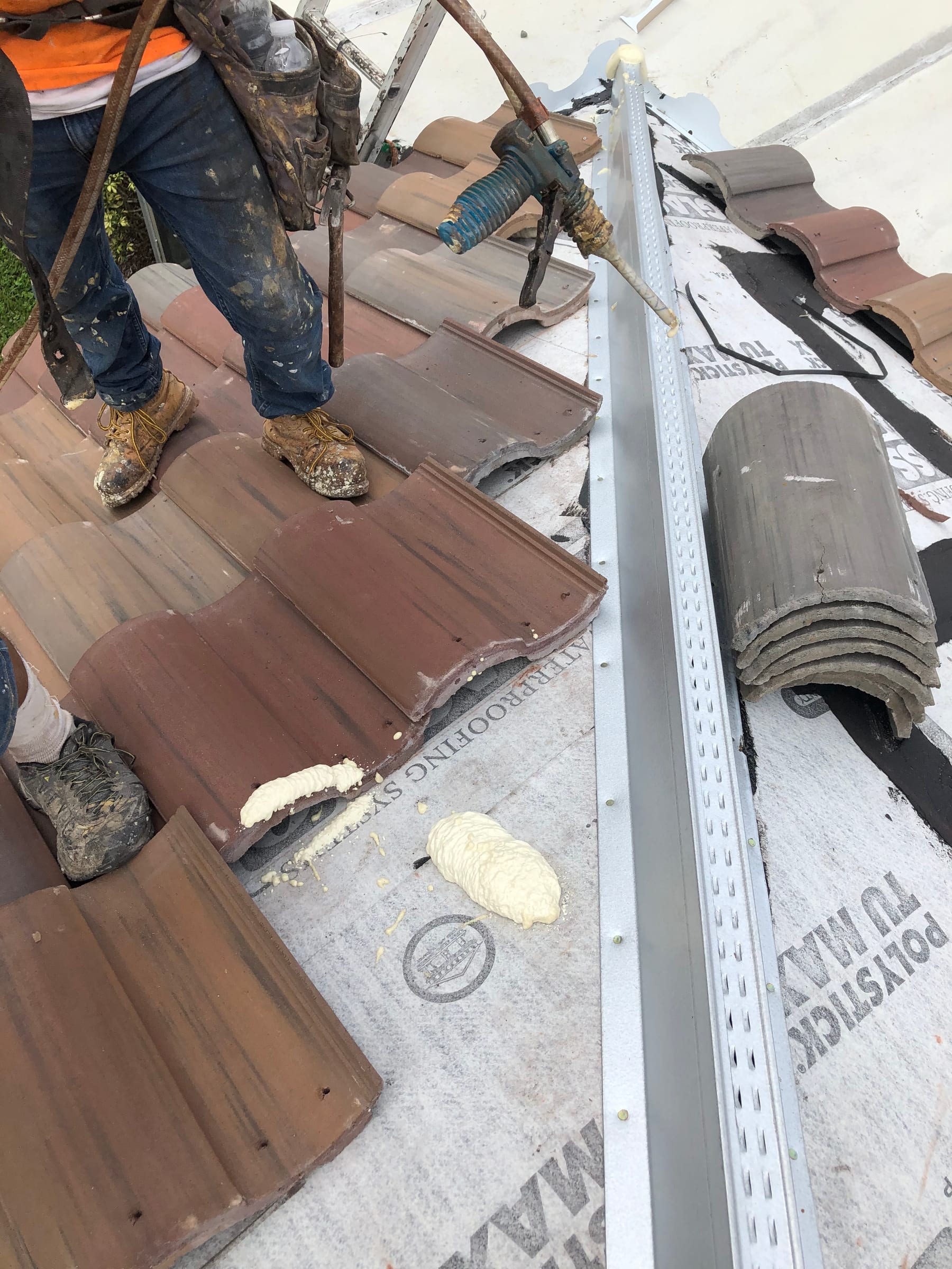 Roofing installer applying foam adhesive during a Barcelona 900 concrete tile installation beside a metal valley.