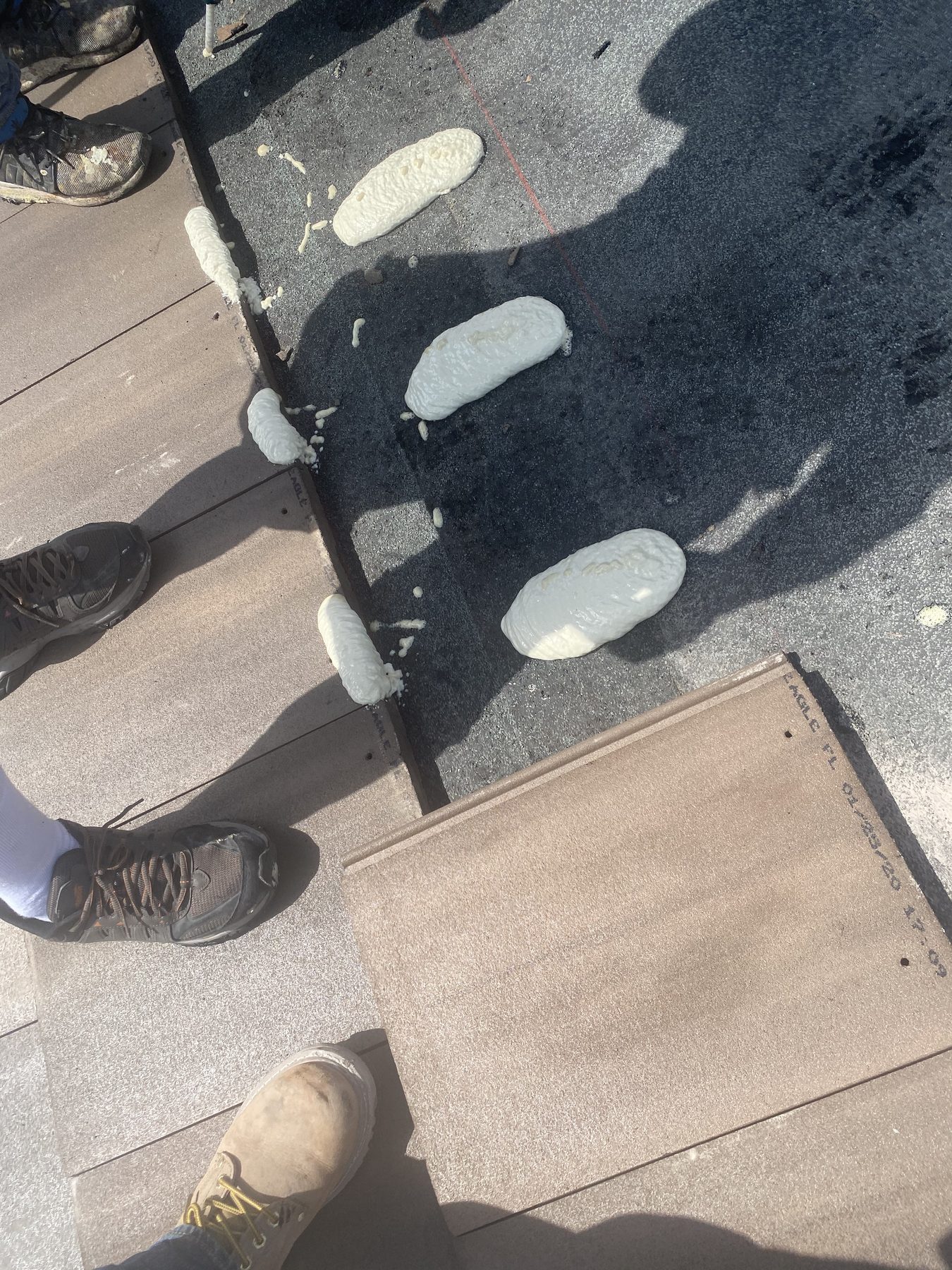 Foam adhesive paddies placed on underlayment beside flat Saxony 900 roof tiles during installation.