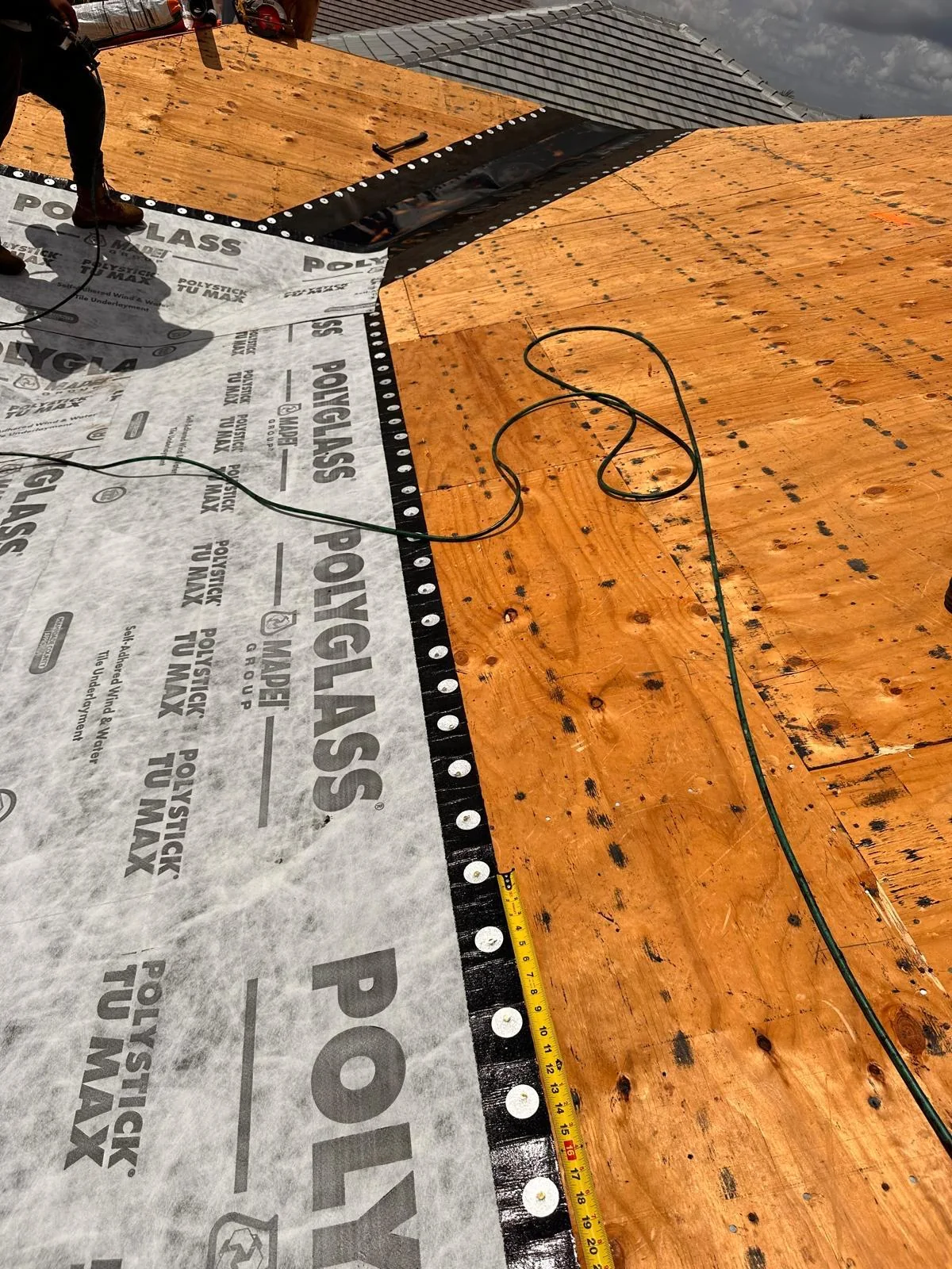Printed Polystick TU MAX membrane with caps and tape beside an exposed section of roof deck