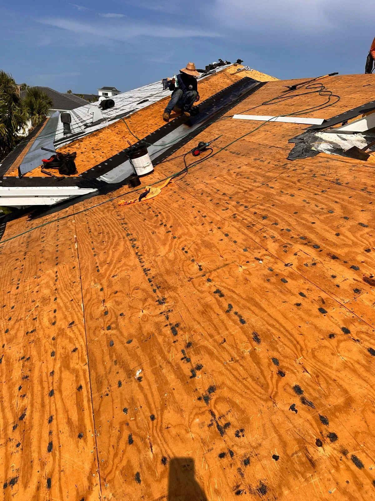 A roofer working along the metal valley with exposed decking and underlayment on the West Palm Beach tile reroof